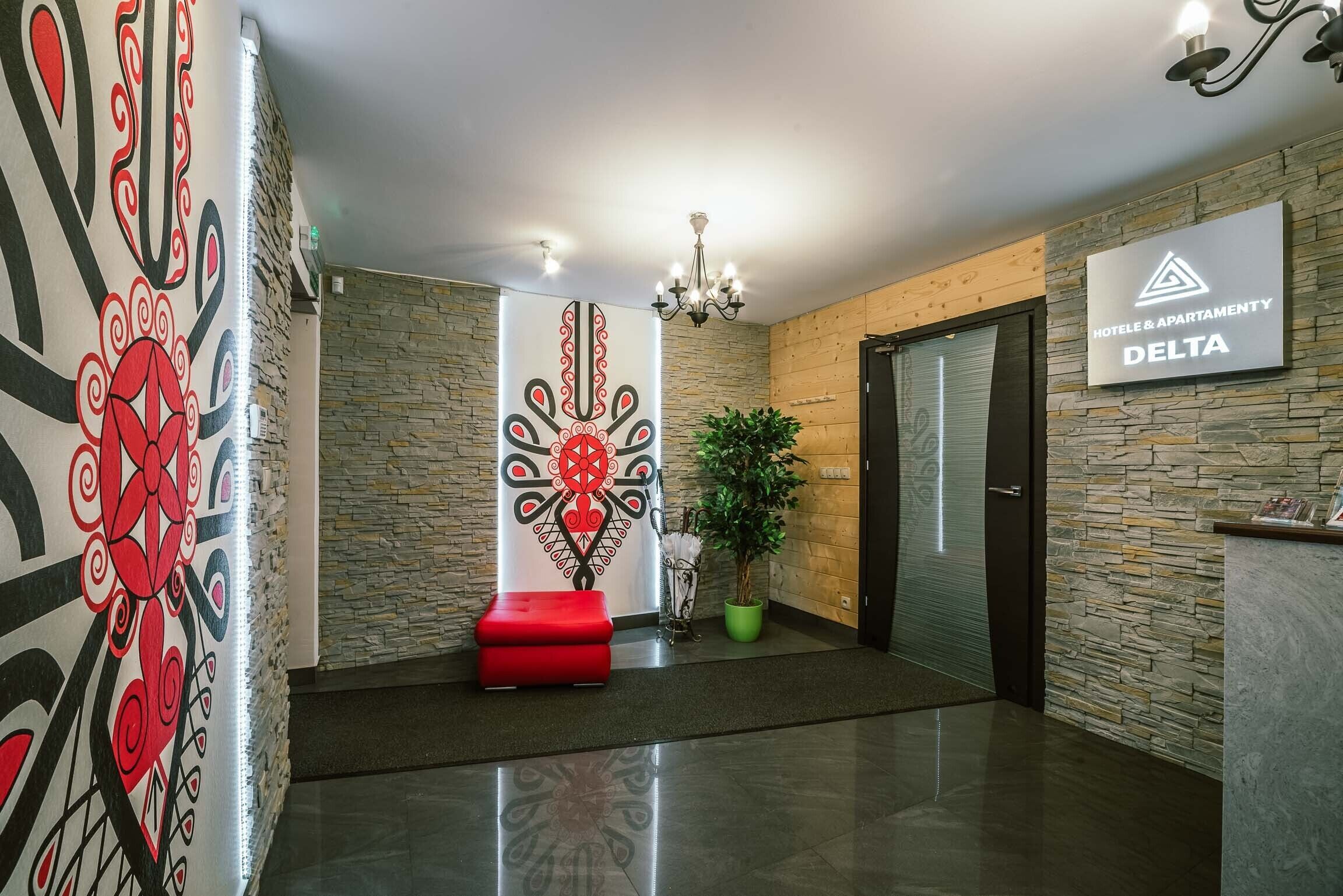 A hotel lobby with a reception desk, a red bench, a decorative wall, and a chandelier.