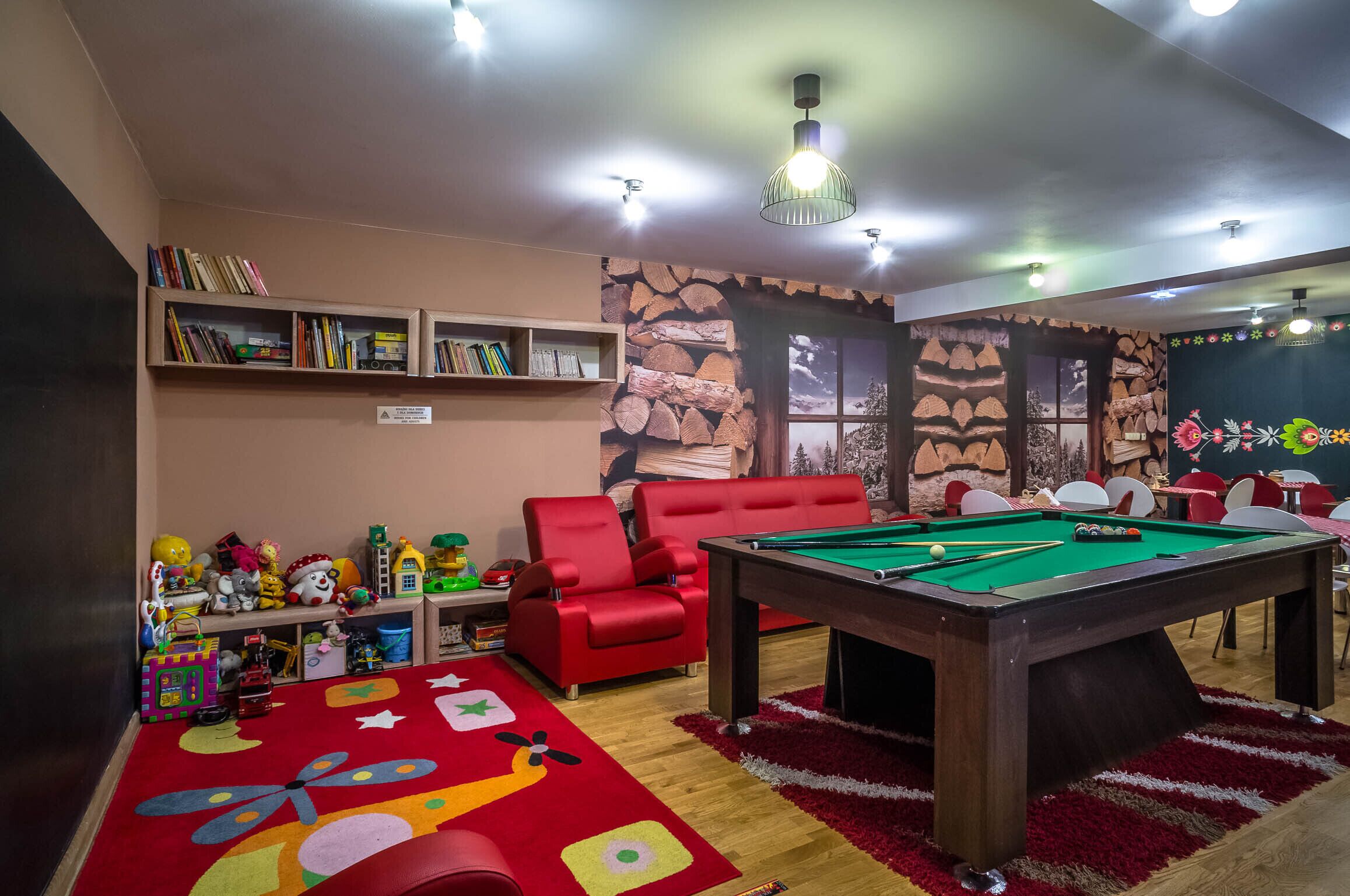 A room with a pool table, red chairs, a bookshelf, and a colorful play mat.