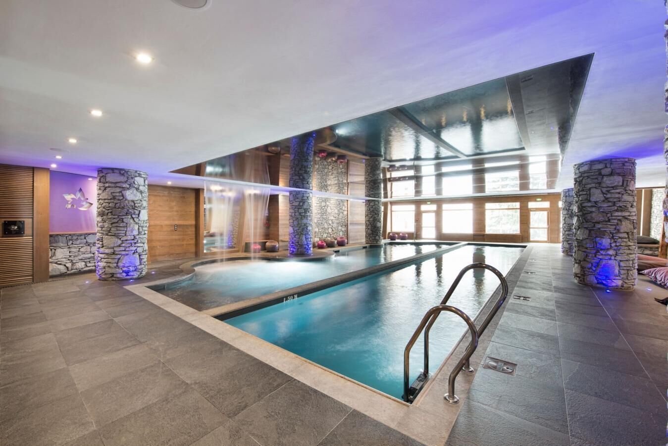Una piscina interior amb pilars de pedra, un mur de pedra i un paviment de fusta.
