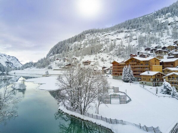 A snow-covered mountain village with wooden buildings, a frozen river, and a clear sky.