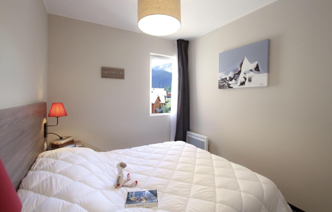 A hotel room with a large bed, a bedside lamp, a window with a view of mountains, and a painting on the wall.