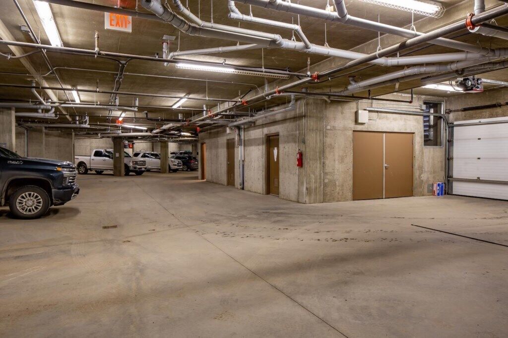 A multi-level parking garage with concrete floors and walls, multiple parking spaces, and overhead pipes.