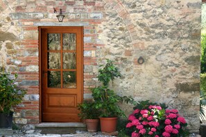 A rustic stone building with a wooden door, potted plants, and a brick wall. - Agriturismo Podere La Cava (San Casciano in Val di Pesa)