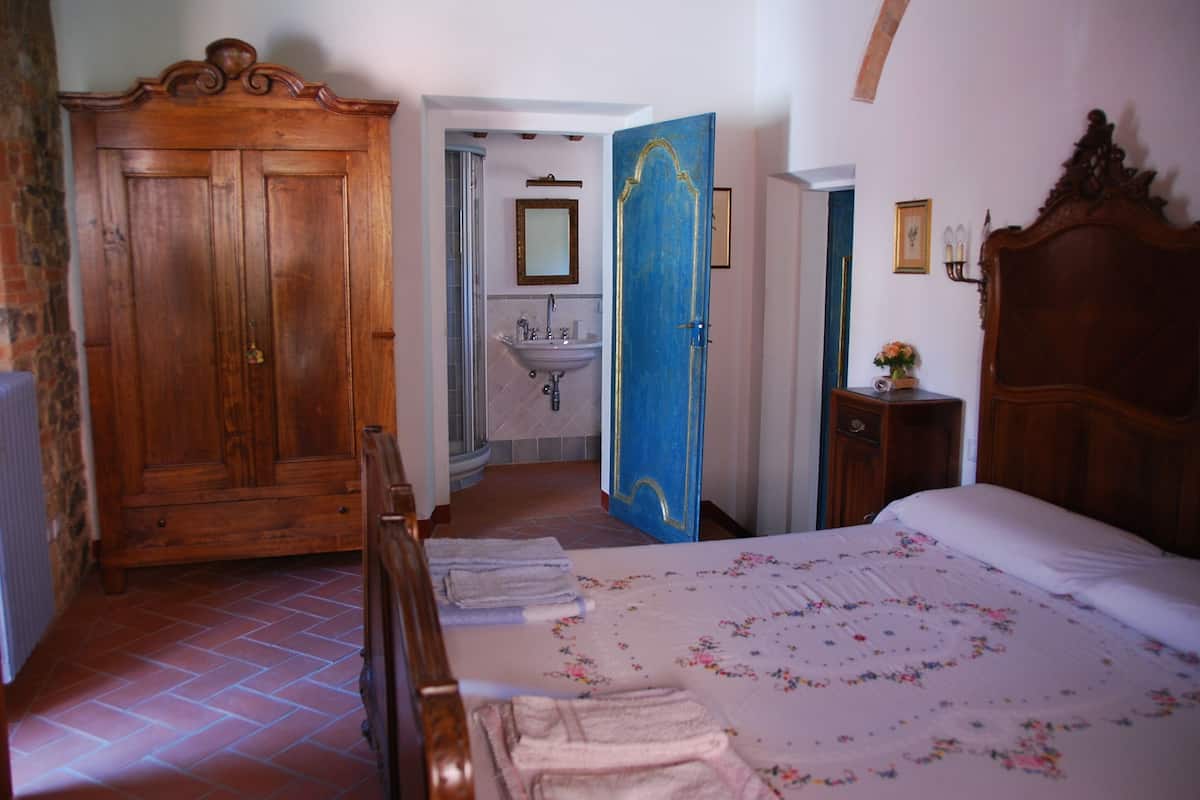 Un dormitorio con un armario de madera, una cama con ropa de cama floral, una puerta azul y un baño con lavamanos y espejo.