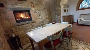 Une cheminée en pierre avec un feu de bois, une table à manger avec des chaises, un canapé et un meuble en bois.