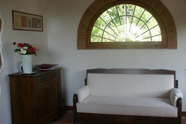 A room with a wooden cabinet, a white sofa, and a window with a view of greenery. - Agriturismo Podere La Cava (San Casciano in Val di Pesa)