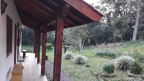 A covered outdoor area with stone flooring, wooden beams, and a garden with various plants and shrubs. - Pousada Heritage Colonial (Nova Petropolis)