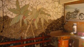 A stone wall with a mosaic, a wooden bench, a table with a coffee machine, and a motorcycle painting. - Pousada Heritage Colonial (Nova Petropolis)