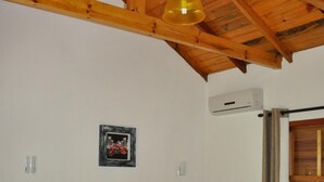 A bedroom with a bed, a hanging light fixture, a wall-mounted air conditioner, and a framed picture. - Pousada Heritage Colonial (Nova Petropolis)