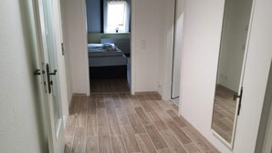 A hallway with wooden flooring leading to a bedroom with a bed and a window. - Apartments am Schloßpark (Senftenberg)