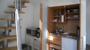 A compact kitchen with a built-in microwave, coffee maker, and a small refrigerator. A wooden staircase is visible to the left, leading to another level. - Apartments am Schloßpark (Senftenberg)