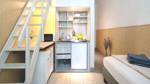 A compact kitchenette with a microwave, sink, and cabinets, a small refrigerator, and a staircase leading to an upper level. - Apartments am Schloßpark (Senftenberg)