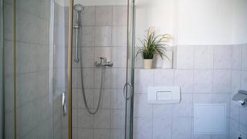 Un baño moderno con ducha envuelta en vidrio, una planta en maceta sobre una estantería y un inodoro con palanca.