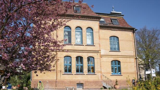 A two-story building with a brick facade, large arched windows, and a visible front entrance. - Apartments am Schloßpark (Senftenberg)