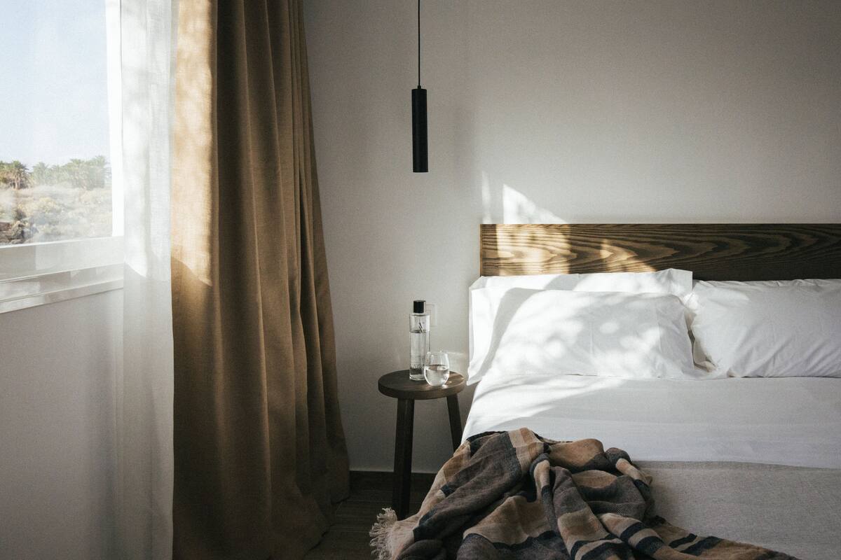 A neatly made bed with white linens, a wooden headboard, and a small bedside table with a bottle and glass.