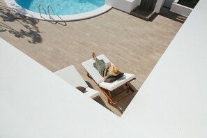 Zona de piscina amb una cadira de gandules, una persona relaxant-se i una piscina amb una escala.