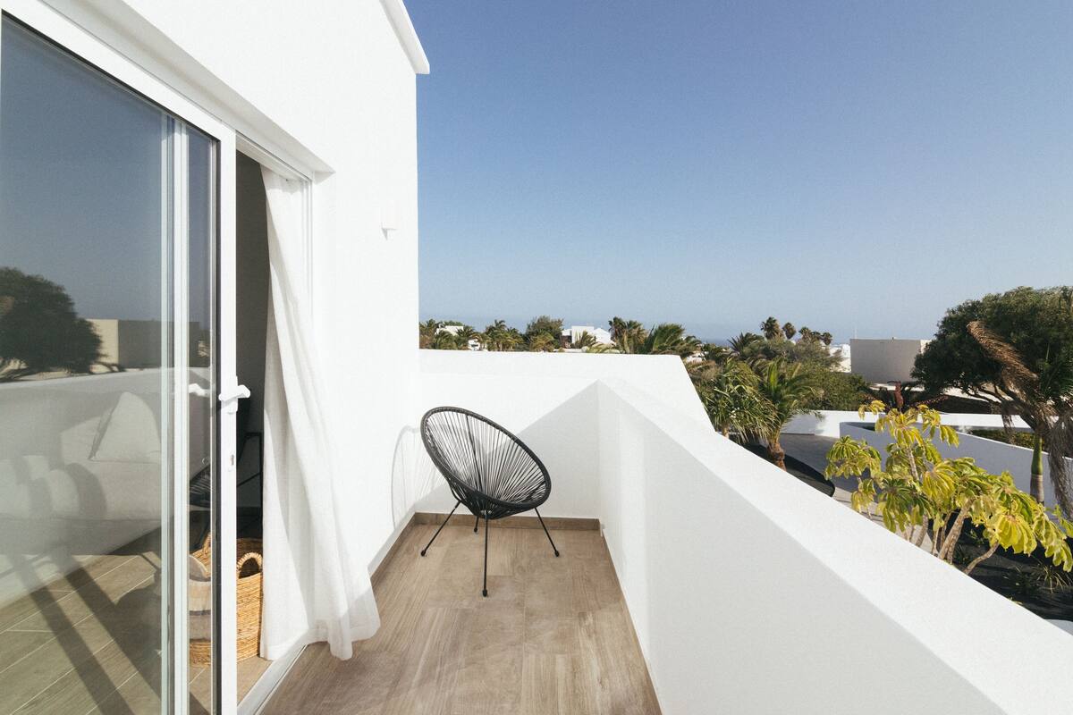 A balcony with a chair, a white wall, and a view of the sea.