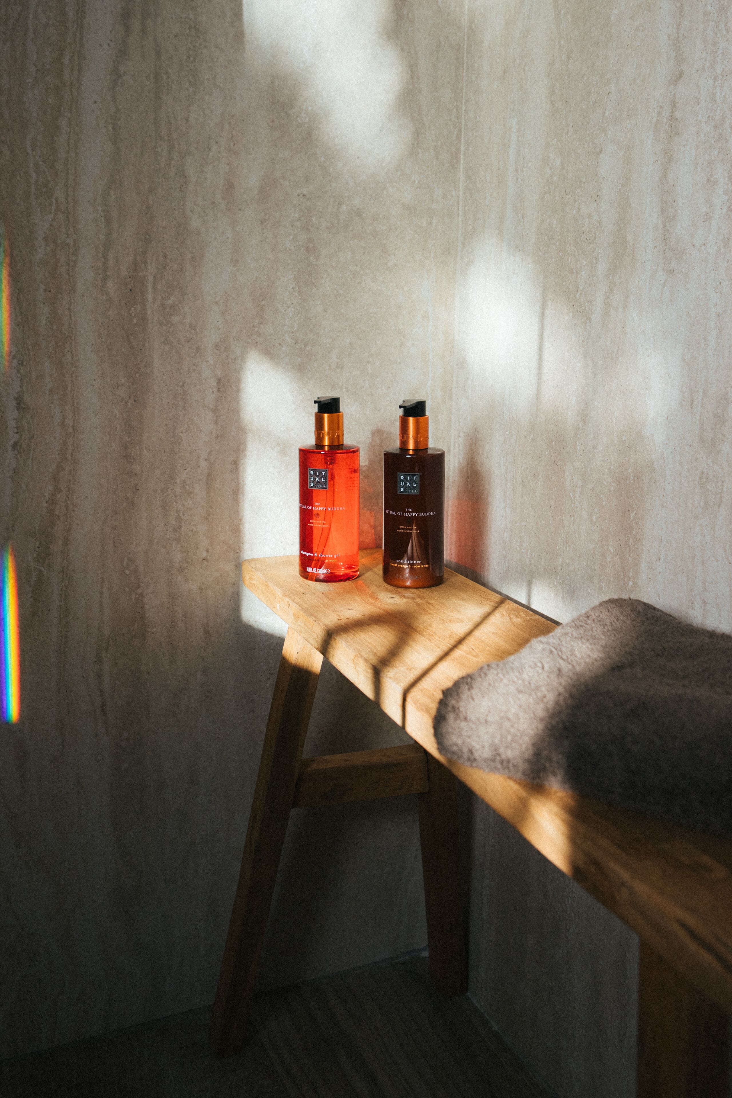 A wooden bench with two bottles of skincare products against a textured wall.