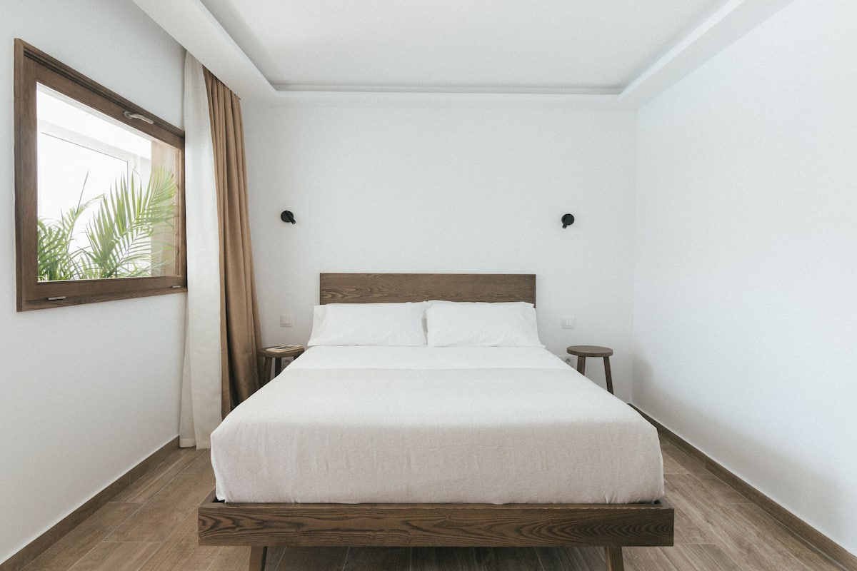 A neatly made bed in a room with a wooden headboard, a nightstand, and a small table.
