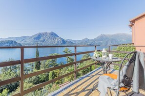 Ein Balkon mit Blick auf einen See und Berge, ein Tisch mit Tasse und Laterne sowie ein Stuhl mit Decke.