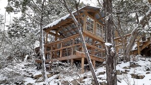 Eine Holzhütte mit mehreren Ebenen, umgeben von schneebedeckten Bäumen und Felsen.