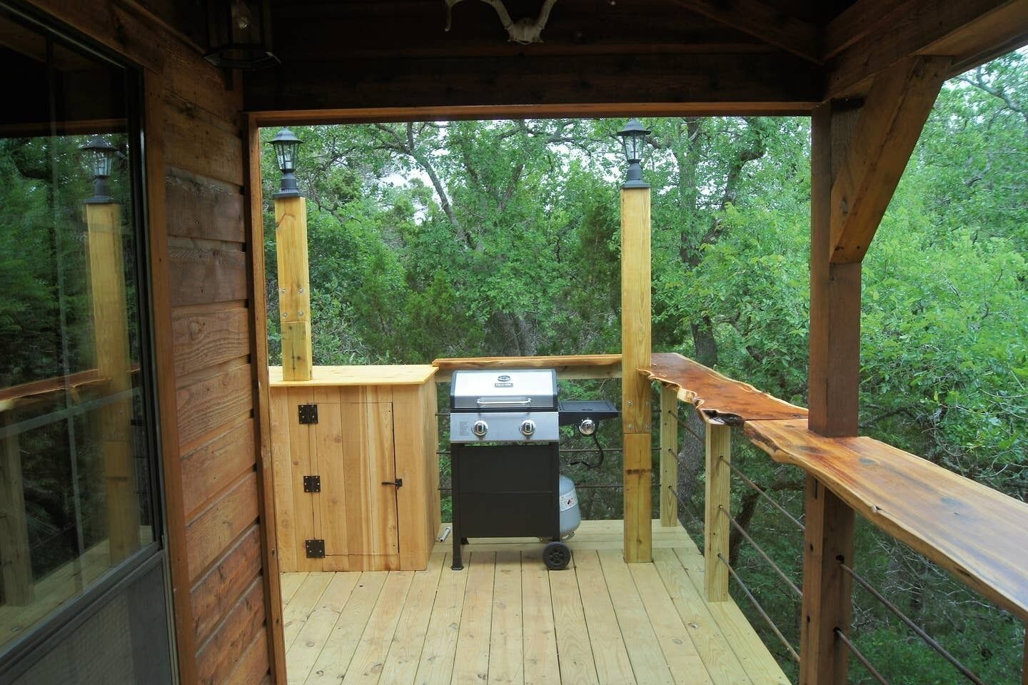Eine Holzterrasse mit Grill, eine Holzhütte und Blick auf einen Wald.
