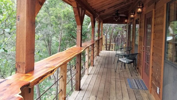 Eine Holzterrasse mit Geländer, Deckenventilator und Tisch mit Stühlen.