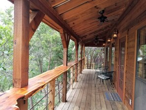 Une terrasse en bois avec une rambarde, un ventilateur de plafond et une table avec des chaises.