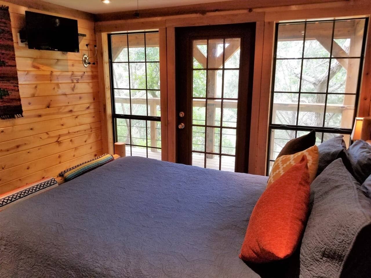 A bedroom with a large bed, a television on the wall, and a view through the door.