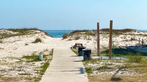 A concrete pathway leading to a beach with a picnic table and trash bins. - TWO POOLS, FISHING PIER, PRIVATE BEACH ACCESS, COZY ACCOMMODATIONS (Gulf Shores)