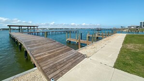 A wooden pier extending into calm waters, with a grassy area beside it and a clear sky above. - TWO POOLS, FISHING PIER, PRIVATE BEACH ACCESS, COZY ACCOMMODATIONS (Gulf Shores)