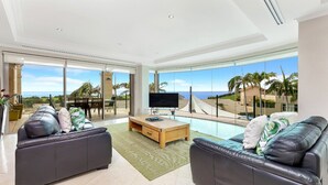 A spacious living room with a large TV, two sofas, a coffee table, and a view of the ocean. - Unit 13 - 3 Bedroom Ocean View (TERRIGAL)