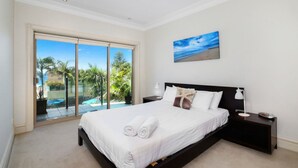 A bedroom with a large bed, a nightstand, a lamp, and a painting of a beach scene. - Unit 13 - 3 Bedroom Ocean View (TERRIGAL)
