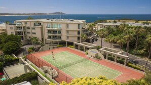 A tennis court surrounded by buildings with a view of the ocean. - Unit 13 - 3 Bedroom Ocean View (TERRIGAL)