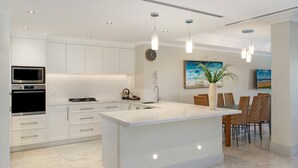 A modern kitchen with white cabinetry, a large island, stainless steel appliances, and pendant lighting.