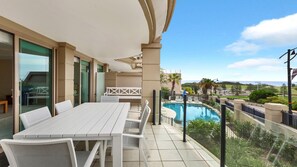 A balcony with a pool, white furniture, and a view of the landscape. - Unit 17 - 3 Bed Part Ocean View (TERRIGAL)