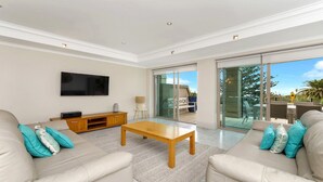 A modern living room with a flat-screen TV, a wooden coffee table, and two sofas with teal cushions.