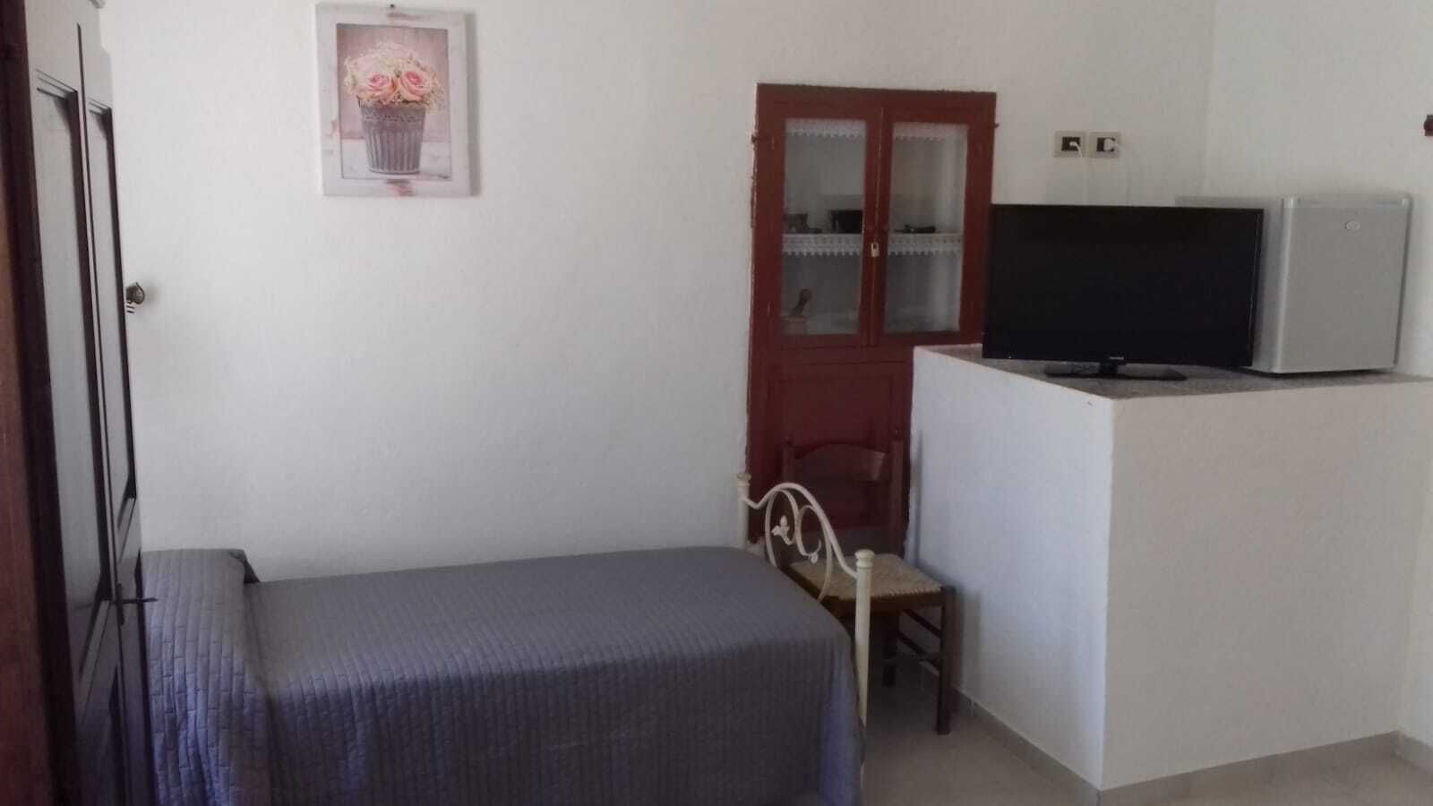 Ein kleines Zimmer mit einem Bett, einem Schreibtisch mit Fernseher, einem Stuhl und einer Tür mit Spiegel.