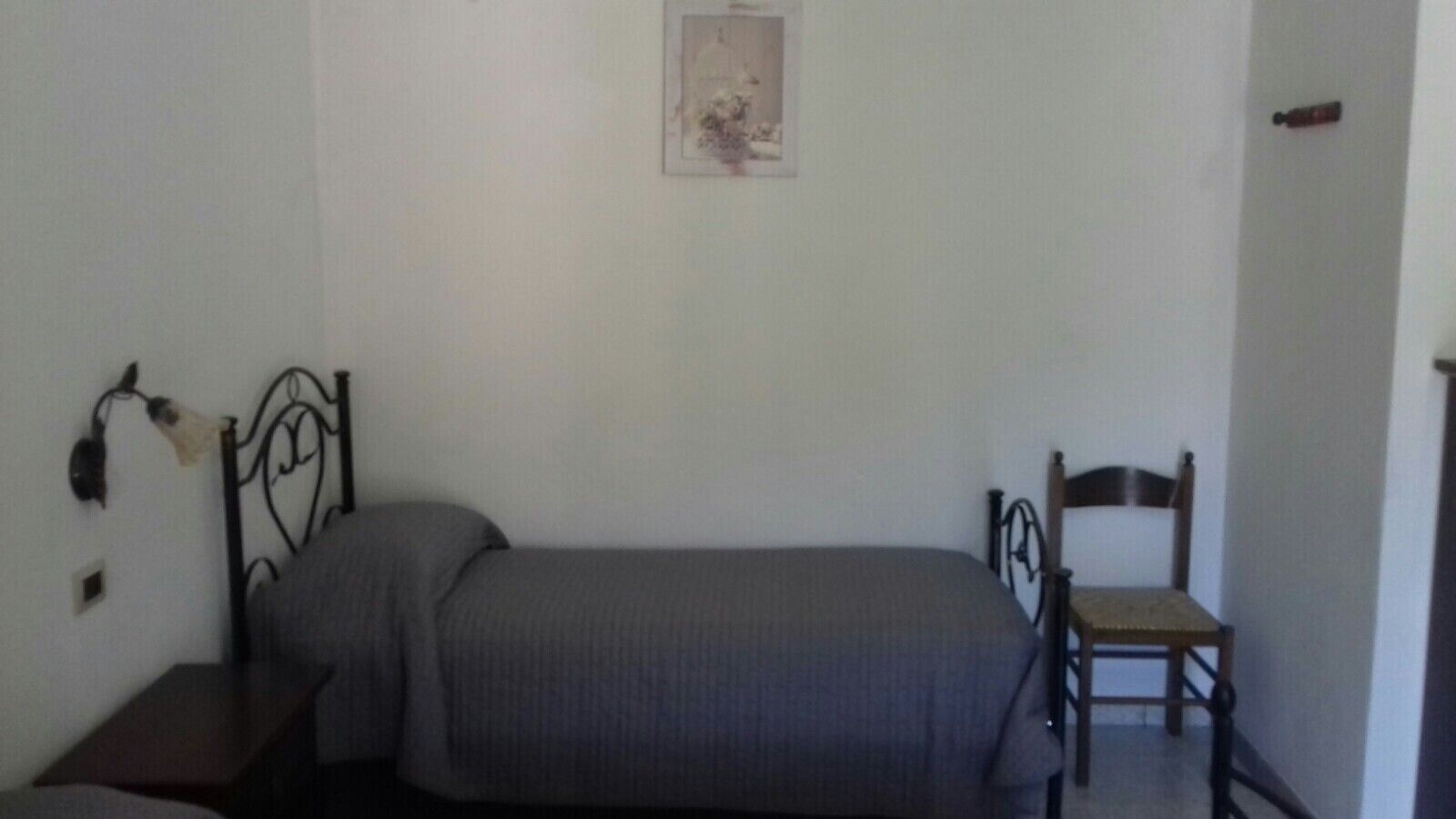 A small, sparsely furnished room with a single bed, a wooden chair, and a small table.