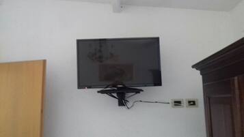 Ein Fernseher an einer weißen Wand, darunter eine sichtbare Steckdose.