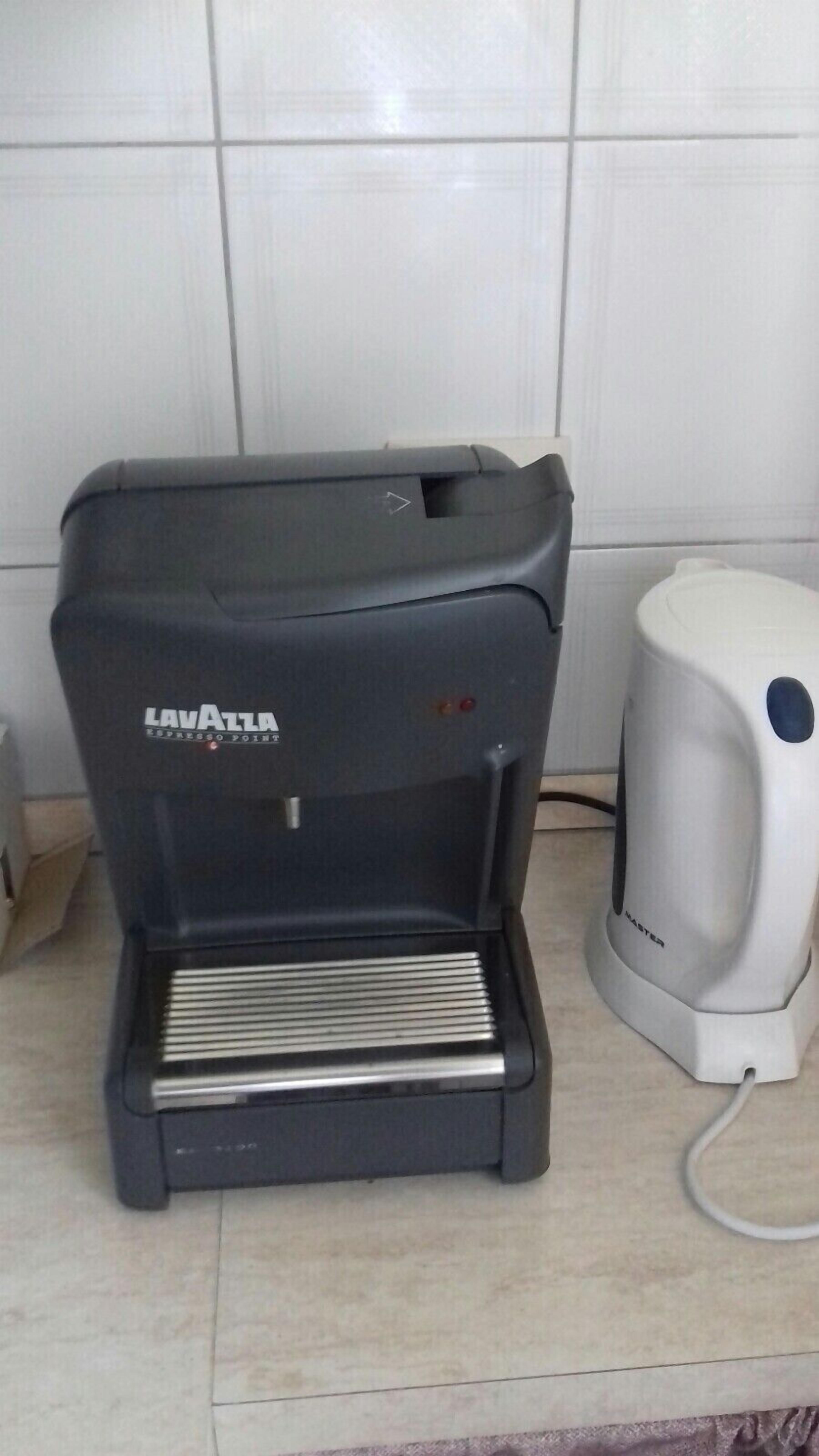 A black Lavazza espresso machine with a drip tray, a coffee maker, and a white base unit.