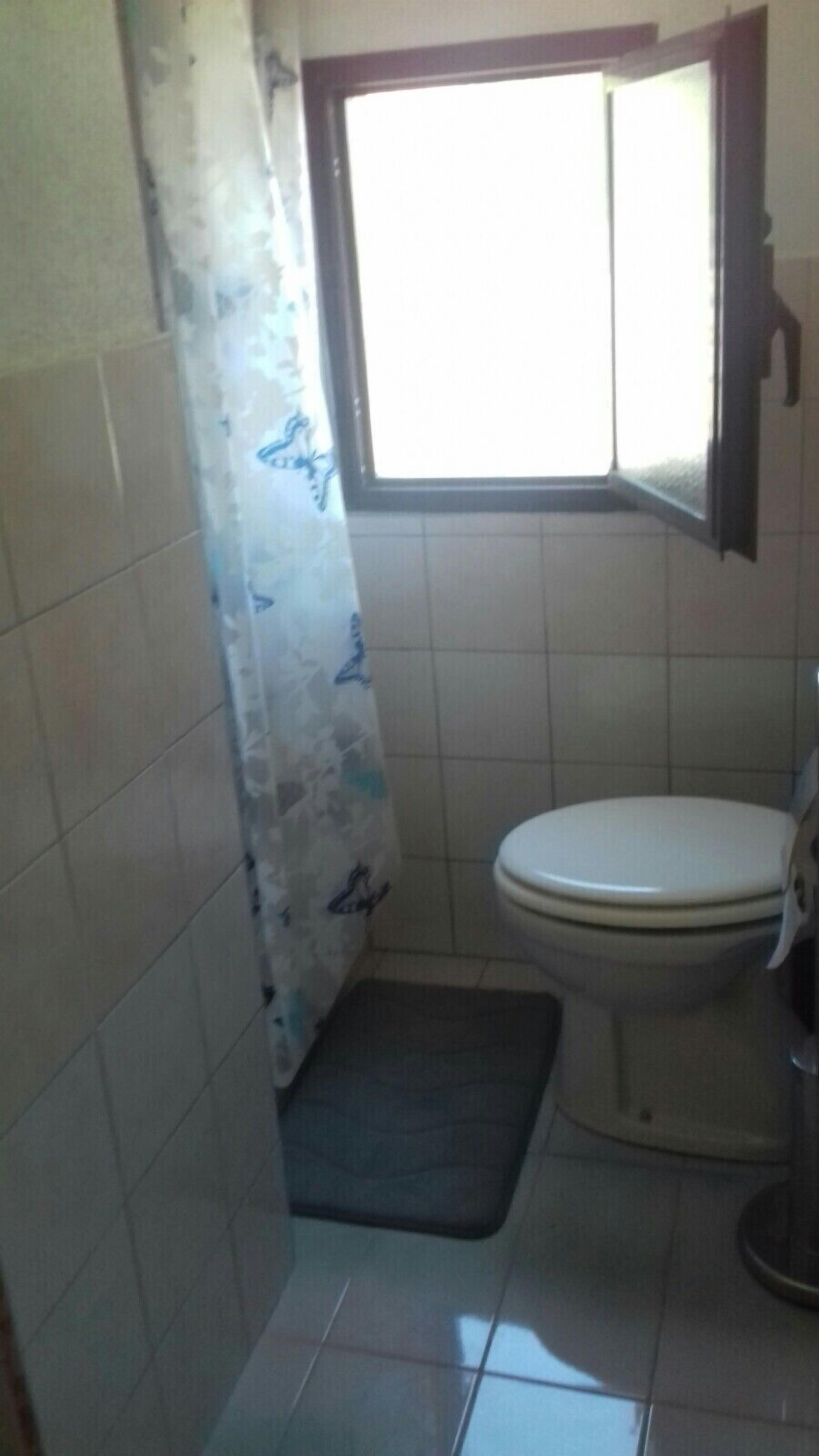 Une petite salle de bain avec des toilettes, un rideau de douche et une fenêtre.