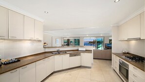A modern kitchen with white cabinetry, a granite countertop, and a view of the ocean. - Unit 25  - 3 Bed Ocean View (TERRIGAL)