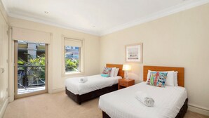 A hotel room with two beds, a balcony, and a window with a view of greenery. - Unit 25  - 3 Bed Ocean View (TERRIGAL)