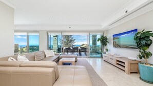 Amplia sala de estar con un sofá grande, una mesa de centro y una zona de comedor con sillas y una mesa. Una ventana grande ofrece vistas al exterior.