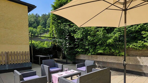 An outdoor patio with wicker furniture, a table, and a large umbrella. - Wonderful private villa for 10 guests with WIFI, TV and terrace (Zell Am See)