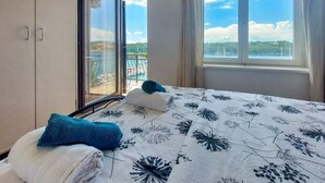 A hotel room with a bed, a window with a view of a body of water and a bridge, and a balcony with a railing. - Lovely apartment for 5 guests with WIFI, A/C, TV, balcony and pets allowed (Rijeka)