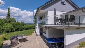 Ein zweistöckiges Haus mit Balkon, Sitzgelegenheit im Freien und Blick ins Grüne.