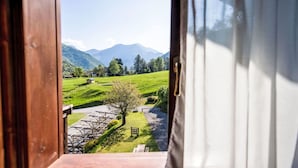 Blick aus einem Fenster, der von einer Holztür aus auf ein grünes Feld mit einem kleinen Gebäude und Bergen in der Ferne zeigt.