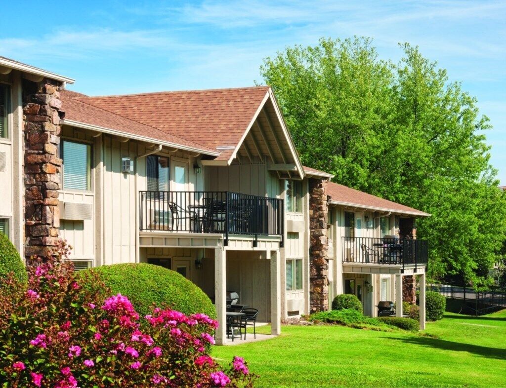 A two-story residential building with a stone facade, multiple balconies, and a well-maintained lawn.